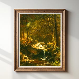 May include: A framed landscape painting depicting a forest scene with a waterfall. The artwork features a warm color palette of greens, browns, and yellows, with sunlight filtering through the trees. The frame is made of wood.