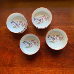 May include: Set of four small white ceramic bowls with a red rim. Each bowl features a colorful bird and floral design.