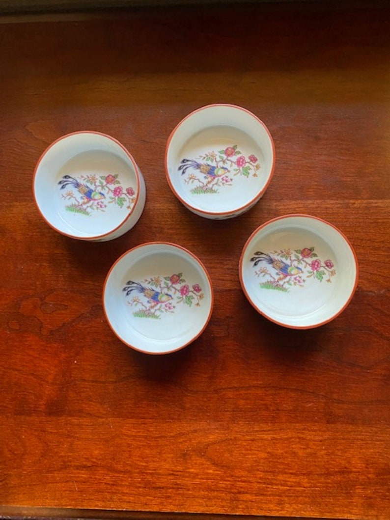 May include: Set of four small white ceramic bowls with a red rim. Each bowl features a colorful bird and floral design.