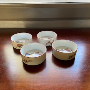May include: Set of four small white porcelain bowls with a floral design. The bowls have a red rim and feature a delicate floral pattern with pink and blue flowers.