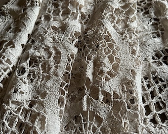 May include: A close-up of a white crocheted lace tablecloth with a delicate floral pattern. The lace is folded in several layers, creating a textured effect.