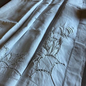 May include: Three white linen pillowcases with delicate embroidered floral designs. The embroidery is intricate and features a variety of stitches.