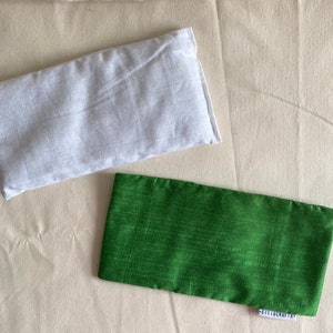 May include: Two rectangular fabric eye pillows. One is white and the other is green.