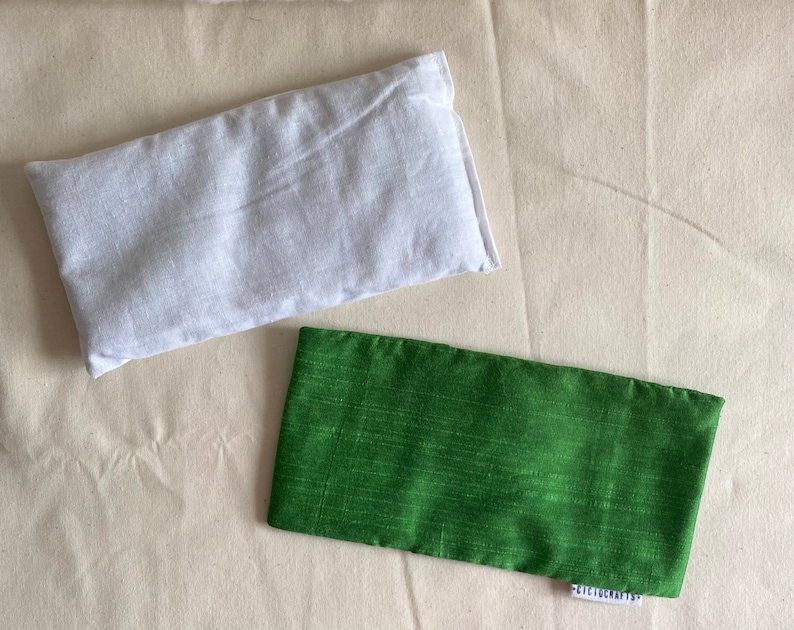 May include: Two rectangular fabric eye pillows. One is white and the other is green.