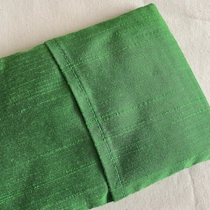 May include: A green fabric pouch with a seam down the center. The fabric has a subtle texture.