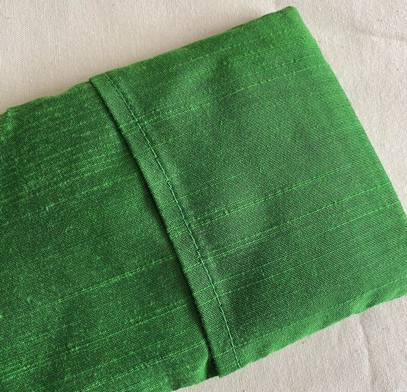 May include: A green fabric pouch with a seam down the center. The fabric has a subtle texture.