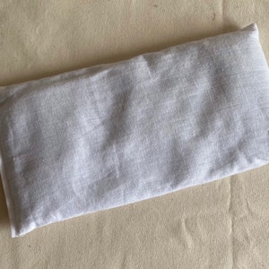 May include: A white linen eye pillow. The pillow is rectangular and has a seam down the center.