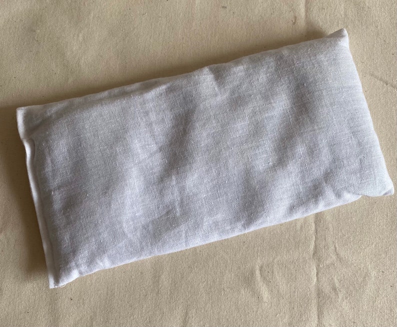 May include: A white linen eye pillow. The pillow is rectangular and has a seam down the center.