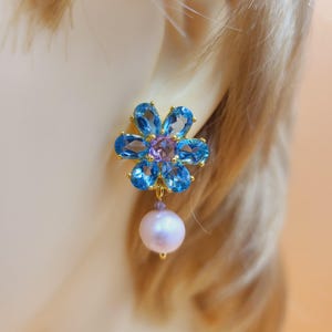 May include: Gold earrings with a blue topaz flower design and a single pearl drop.