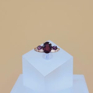 May include: A rose gold ring with a large oval-shaped purple gemstone and two smaller purple gemstones on either side.