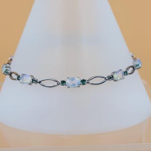 Könnte beinhalten: Ein silbernes Armband mit ovalen weißen Opalen und kleinen grünen Edelsteinen.