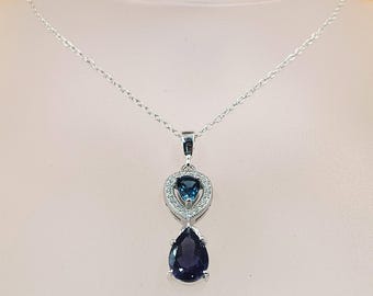 May include: A silver pendant necklace featuring a teardrop-shaped, dark blue gemstone below a heart-shaped, light blue gemstone surrounded by small, clear stones. The necklace hangs on a delicate silver chain.