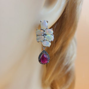 May include: Silver dangle earrings featuring a cluster of white opal stones and a single red teardrop-shaped gemstone.