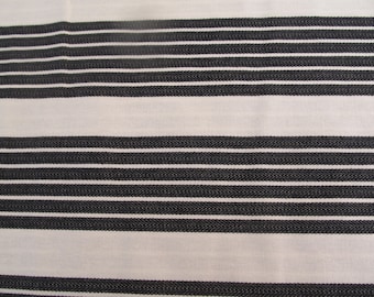 May include: Close-up of a white fabric with evenly spaced, horizontal black stripes. The stripes have a textured appearance, creating a subtle pattern. The fabric appears to be a woven material, possibly cotton or linen.
