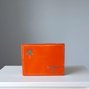 May include: Orange rectangular box with gold trim and the text "State Express 777" printed on the front. The box has a small crest with the text "Absolutely unique" printed on the top.