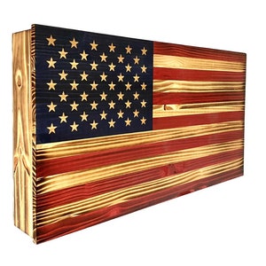 May include: A wooden American flag with red, white, and blue paint. The flag is made of reclaimed wood and has a rustic look. The flag is mounted on a wooden frame.
