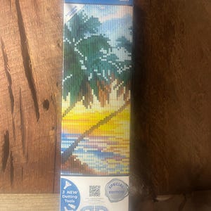 May include: A Diamond Dotz kit featuring a tropical sunset scene. The box displays a pixelated image of palm trees, a yellow and orange sunset, and water. The kit includes 3 new dotting tools and is a special edition.