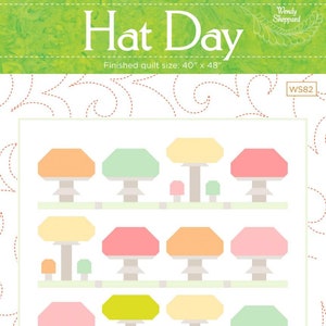 Könnte beinhalten: Ein Quiltmuster mit dem Titel "Hat Day" mit bunten Pilzdesigns. Die fertige Quiltgröße beträgt 101,6 cm x 121,9 cm. Die Pilze sind in Orange-, Grün-, Gelb- und Rosatönen gehalten. Der Hintergrund ist weiß.