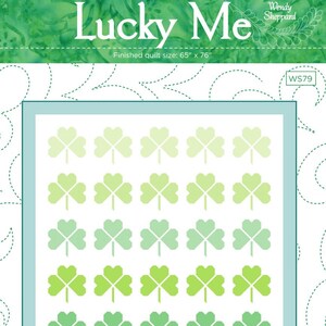 May include: A quilt pattern with the text "Lucky Me" and shamrock designs. The finished quilt size is 65" x 76". The shamrocks are in shades of green on a white background, framed by a light blue border.