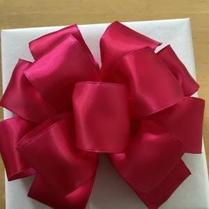 May include: A large, bright pink satin bow tied on top of a white gift box.