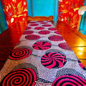 Puede incluir: Un camino de mesa con un patrón de diseños de piruletas giratorias en rosa, negro y blanco. El camino de mesa está sobre una mesa de madera.