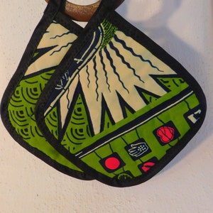 May include: A pair of green and white pot holders with black trim. The pot holders have a geometric pattern with red and black accents.