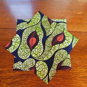 May include: Two folded fabric napkins with a green, white, and blue leaf pattern. The leaves have a red center and are outlined in black.