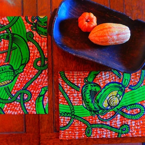 Puede incluir: Dos manteles individuales naranja y verde con un patrón de auriculares y cables. Los manteles individuales están sobre una mesa de madera con un cuenco de madera y dos calabazas.