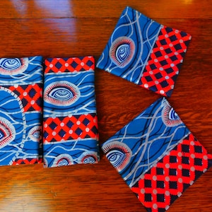Puede incluir: Cuatro posavasos de tela azul y rojo con un diseño de ojo blanco. Los posavasos tienen un patrón de diamante en el borde inferior.