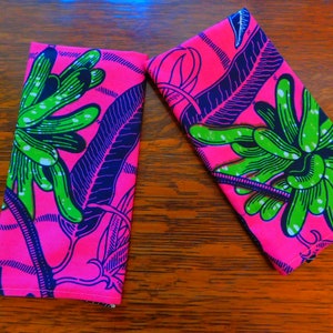 Puede incluir: Dos servilletas de tela rosa con un patrón floral verde y azul. Las servilletas están dobladas y colocadas sobre una superficie de madera.