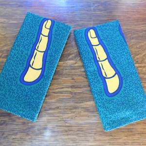 Puede incluir: Dos bolsas de tela verde con un diseño de dedo azul y amarillo. Las bolsas tienen un patrón repetitivo de garabatos azules sobre un fondo verde.