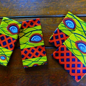 Puede incluir: Conjunto de cuatro servilletas de tela amarillas, verdes, rojas y azules con un patrón repetido de ojos estilizados y un patrón de diamantes.