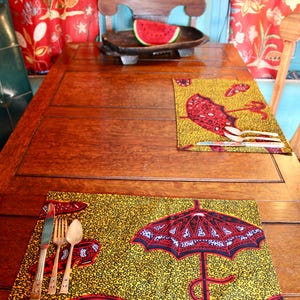 Puede incluir: Dos manteles individuales rectangulares con fondo amarillo, patrón de remolinos negros y un gráfico de paraguas rojo. Cada mantel tiene un cuchillo, tenedor y cuchara plateados, dispuestos sobre una mesa de madera marrón oscura.