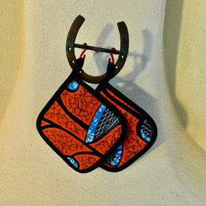 May include: Two orange and blue patterned fabric pot holders hanging from a rusty horseshoe.