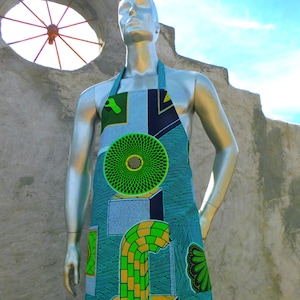 Puede incluir: Un maniquí plateado que lleva un delantal estampado en azul, verde y amarillo con diseños geométricos. El delantal tiene un círculo verde grande con un círculo amarillo más pequeño en el centro.