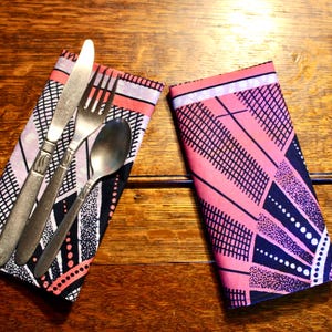 May include: A set of vintage silverware, including a knife, fork, and spoon, rests on a patterned napkin. The napkin features a geometric design in pink, black, and white. A second napkin with a similar design is next to the silverware.