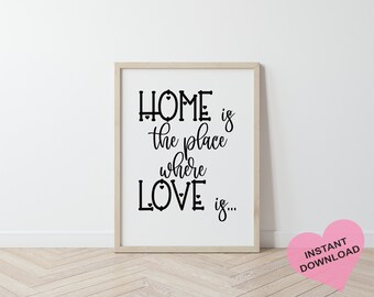 May include: A black and white printable wall art print with the text "Home is the place where love is..." in a decorative font. The print is framed in a light wood frame and is displayed on a white wall.