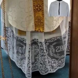 May include: Close-up of a religious garment with intricate white lace detailing. The garment features a gold-colored band with ornate patterns and a cross design. A small image of a light gray shirt is in the upper right corner.