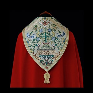 May include: A white and gold embroidered stole with a floral design and a red background. The stole has a tassel at the bottom.