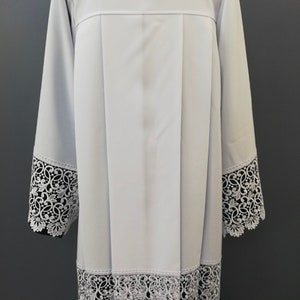 May include: White liturgical alb with lace trim around the sleeves and bottom hem.