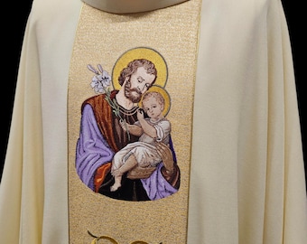 May include: A white liturgical vestment with a gold embroidered panel featuring Saint Joseph holding the baby Jesus. The panel has a decorative floral design at the bottom.
