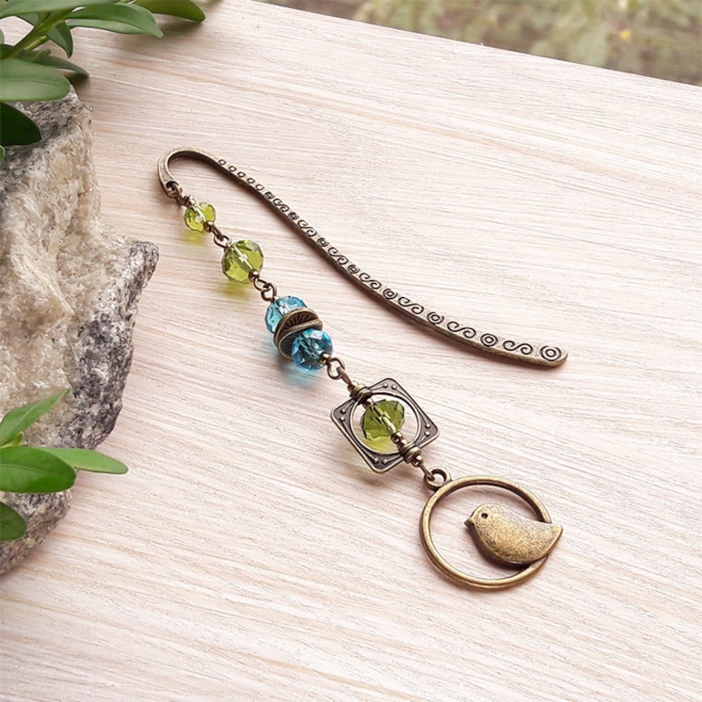 May include: A bronze bookmark with a green and blue glass bead chain, a square charm with a green glass bead, and a bird charm.