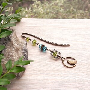 May include: A bronze bookmark with a small bird charm, green and blue glass beads, and a decorative metal charm.