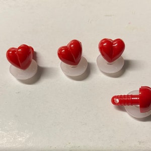 May include: Four red plastic heart-shaped buttons with white plastic backing. The buttons have a small hole in the center for sewing.