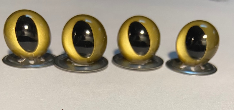 May include: Four gold plastic safety eyes with black pupils, each mounted on a silver washer.