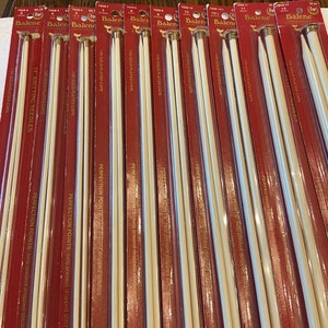 May include: A close-up of a set of 14 knitting needles with gold-plated caps. The needles are packaged in red and white packaging with the brand name "Balene" printed on the front. The packaging also includes the text "Perfection Points help prevent dropped stitches".