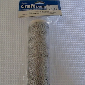 May include: A spool of silver metallic cord, 50 yards, for crafting. The label reads "Craft Design" and "High Quality Essentials for Creative Projects".