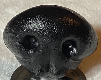 May include: Black plastic animal nose with two nostrils. The nose is textured and has a rounded shape.