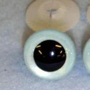 May include: Two light blue plastic doll eyes with black pupils. The eyes are round and have a shiny finish.