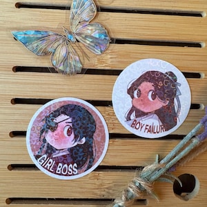 May include: Two round stickers with cartoon illustrations of a girl and a boy. The girl sticker has the text "Girl Boss" and the boy sticker has the text "Boy Failur".